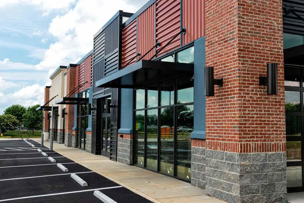 Modern commercial building exterior featuring metal panel siding, brick veneer, large storefront windows, and covered walkways